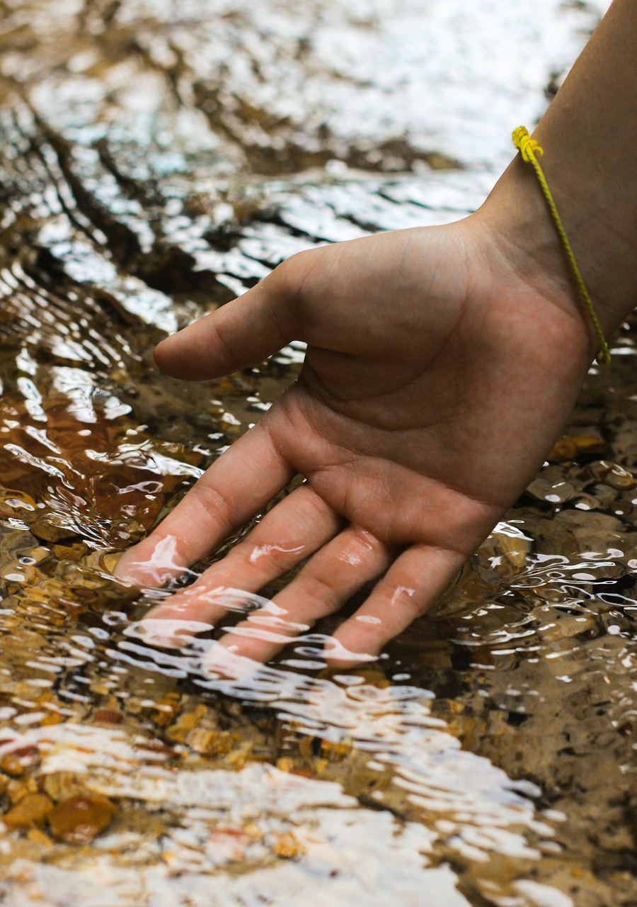 Hand berührt klares Wasser in einem Gebirgsbach